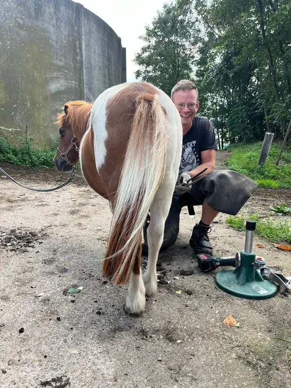 Andre Schnackenberg kniet neben einem Schecken-Pony am Hufbock